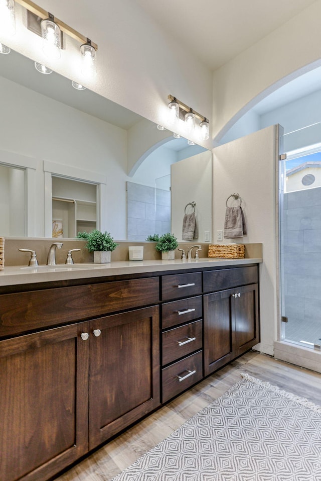 bathroom with a sink, double vanity, wood finished floors, and a shower stall