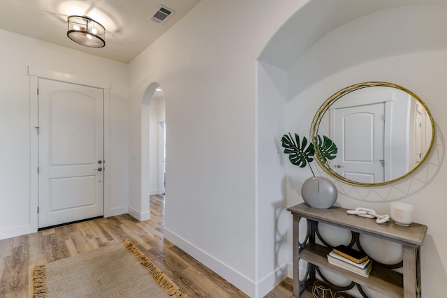 foyer entrance with arched walkways, light wood-type flooring, visible vents, and baseboards