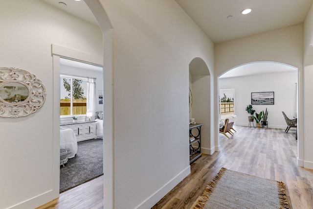 corridor with arched walkways, light wood finished floors, recessed lighting, and baseboards