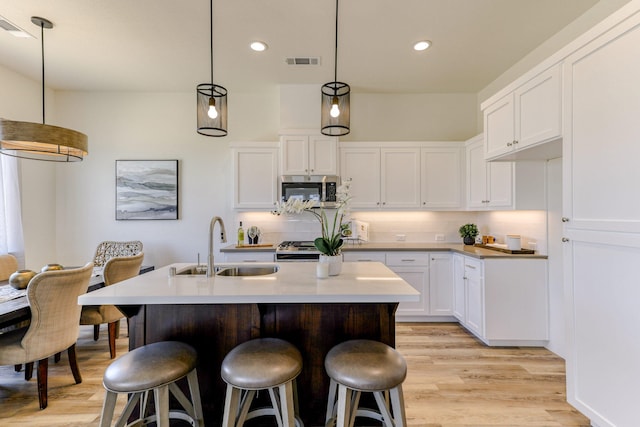 kitchen featuring light wood finished floors, visible vents, stainless steel microwave, a breakfast bar, and a sink