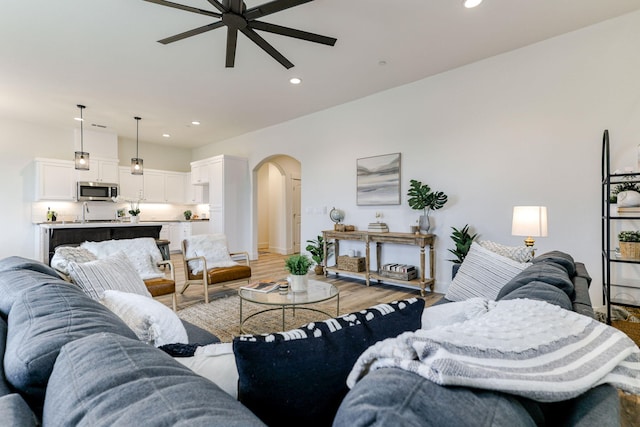 living area with arched walkways, ceiling fan, recessed lighting, and light wood-style floors