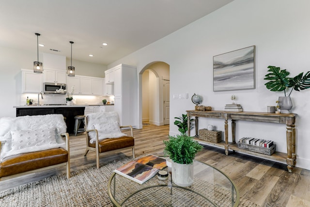 living room featuring light wood finished floors, visible vents, arched walkways, baseboards, and recessed lighting