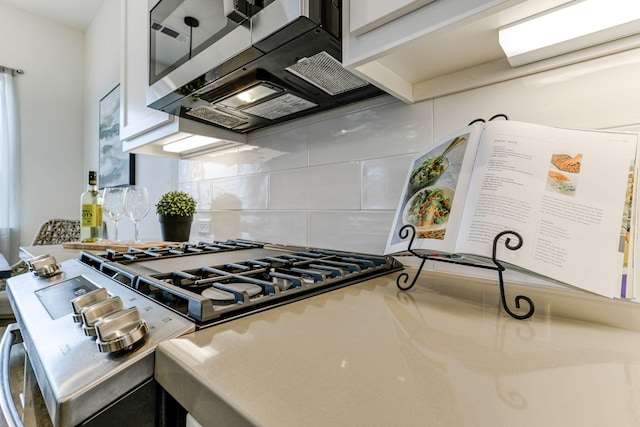 kitchen with stovetop, stainless steel microwave, backsplash, and white cabinetry