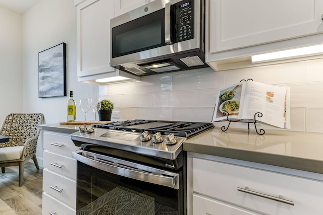 kitchen featuring white cabinets, light wood finished floors, stainless steel appliances, and backsplash