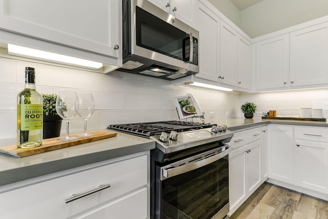 kitchen featuring appliances with stainless steel finishes, light wood-type flooring, backsplash, and white cabinetry