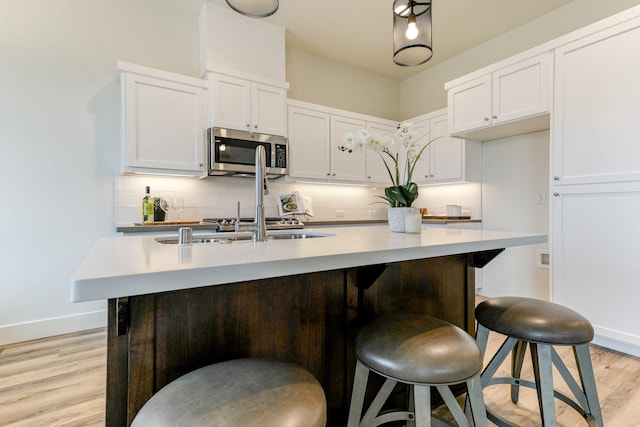 kitchen with light countertops, stainless steel microwave, light wood-style flooring, decorative backsplash, and white cabinetry