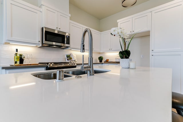 kitchen with a sink, white cabinetry, light countertops, decorative backsplash, and stainless steel microwave