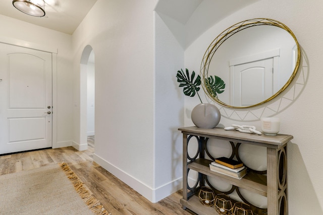 foyer entrance with light wood-type flooring, baseboards, and arched walkways