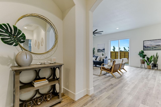 corridor with light wood-style floors, baseboards, arched walkways, and recessed lighting