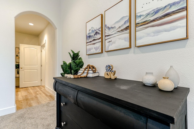 hallway with arched walkways, light carpet, and baseboards