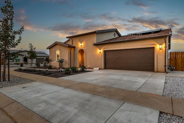 mediterranean / spanish home featuring an attached garage, fence, concrete driveway, roof mounted solar panels, and stucco siding