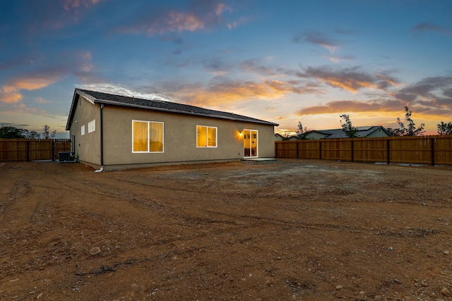 back of house at dusk with central air condition unit, a fenced backyard, and stucco siding