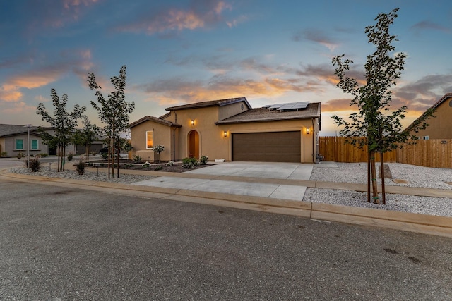 view of front of home featuring a garage, fence, driveway, roof mounted solar panels, and stucco siding