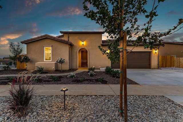 mediterranean / spanish house featuring a garage, a tile roof, fence, driveway, and stucco siding