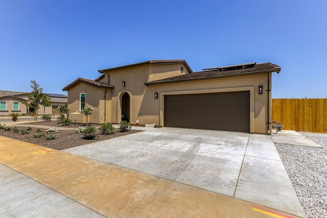 mediterranean / spanish home with an attached garage, fence, concrete driveway, roof mounted solar panels, and stucco siding