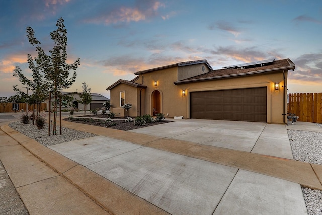 mediterranean / spanish house featuring stucco siding, solar panels, an attached garage, fence, and driveway