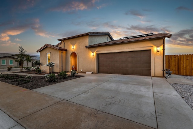 mediterranean / spanish home featuring an attached garage, fence, concrete driveway, roof mounted solar panels, and stucco siding