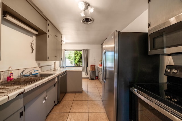 kitchen with light tile patterned floors, visible vents, tile counters, appliances with stainless steel finishes, and backsplash