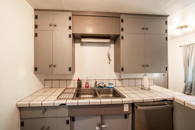 kitchen featuring a sink, tile countertops, gray cabinets, and stainless steel dishwasher