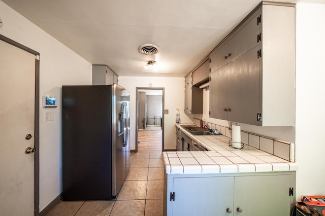 kitchen with tile countertops, light tile patterned floors, visible vents, a sink, and stainless steel fridge