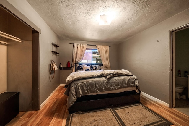 bedroom with a textured wall, a textured ceiling, baseboards, and wood finished floors