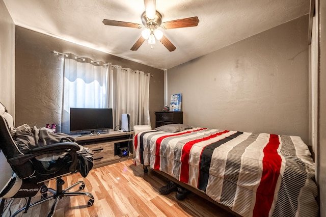 bedroom featuring lofted ceiling, light wood-style flooring, ceiling fan, and a textured wall