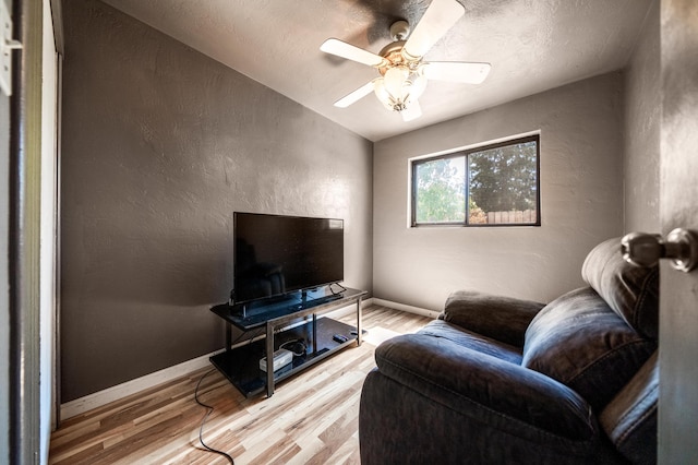 living area with ceiling fan, a textured wall, light wood-style flooring, and baseboards