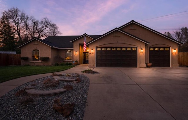 ranch-style home with driveway, a lawn, an attached garage, fence, and stucco siding