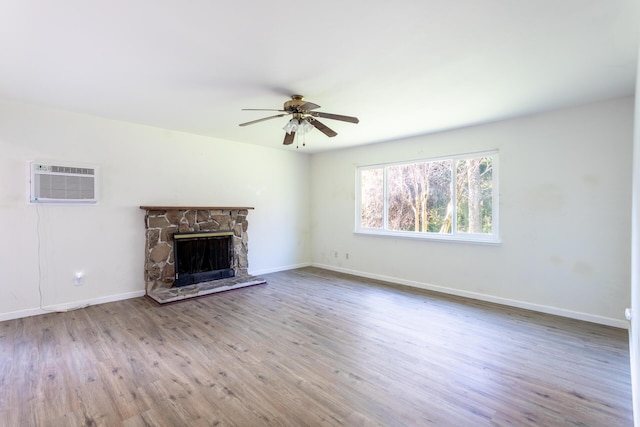 unfurnished living room with a wall unit AC, a fireplace, a ceiling fan, wood finished floors, and baseboards