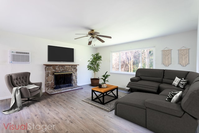 living area featuring light wood-type flooring, a stone fireplace, a wall mounted air conditioner, and baseboards