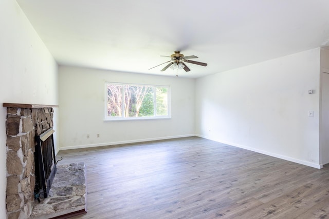 unfurnished living room featuring ceiling fan, baseboards, wood finished floors, and a stone fireplace