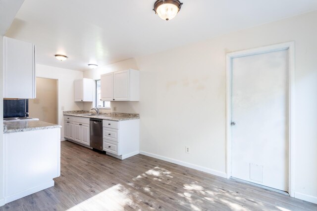 kitchen featuring light wood-style flooring, white cabinetry, baseboards, light countertops, and stainless steel dishwasher