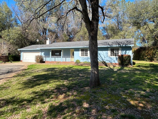 ranch-style home featuring a porch, a chimney, an attached garage, and a front yard