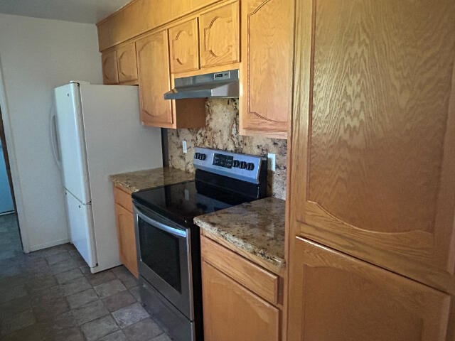 kitchen featuring light stone counters, under cabinet range hood, freestanding refrigerator, decorative backsplash, and stainless steel electric range oven