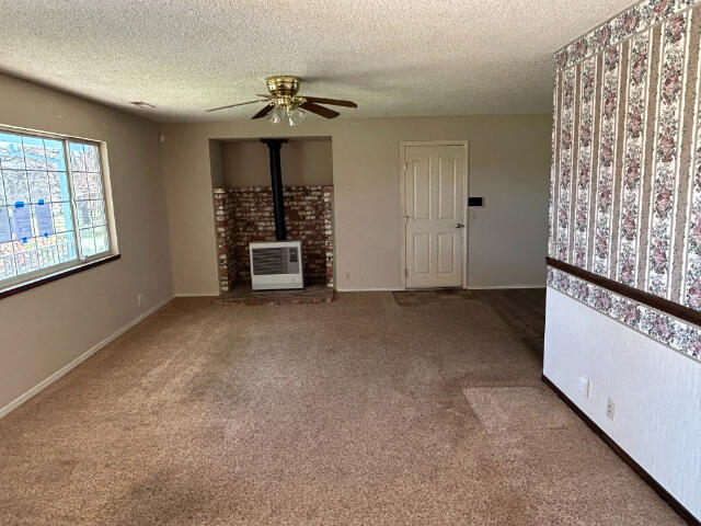 unfurnished living room with a ceiling fan, a wood stove, heating unit, a textured ceiling, and carpet floors