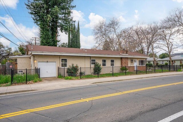 ranch-style house with a fenced front yard, stucco siding, a chimney, driveway, and an attached garage