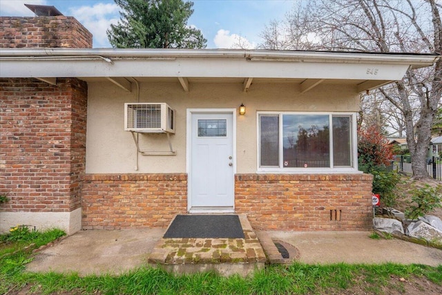 property entrance featuring a wall unit AC, brick siding, and stucco siding