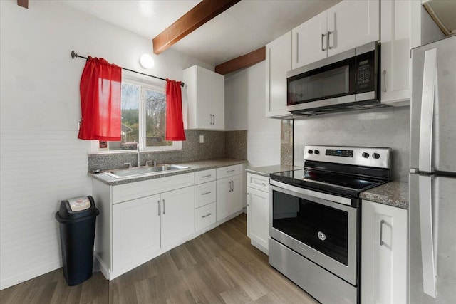 kitchen with wood finished floors, beam ceiling, a sink, stainless steel appliances, and white cabinets