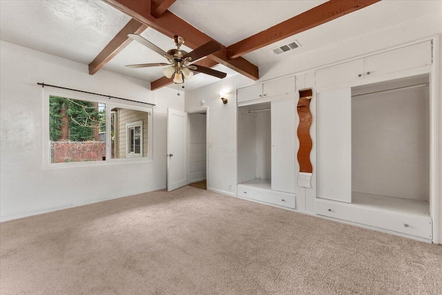 unfurnished bedroom with carpet, baseboards, visible vents, beam ceiling, and a textured ceiling