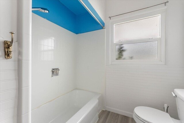 bathroom featuring baseboards, toilet, a tub to relax in, wood finished floors, and a shower