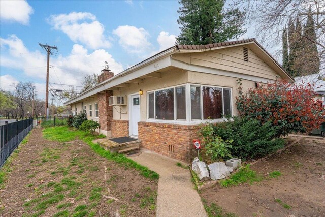 view of front of house featuring stucco siding, a wall unit AC, fence, brick siding, and a chimney