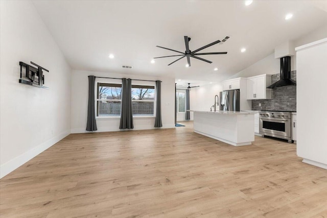 kitchen with stainless steel appliances, white cabinetry, vaulted ceiling, decorative backsplash, and wall chimney exhaust hood