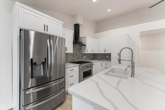 kitchen featuring decorative backsplash, wall chimney exhaust hood, light stone countertops, stainless steel appliances, and a sink