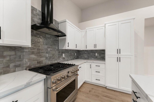 kitchen with white cabinetry, light wood-style floors, wall chimney range hood, high end stainless steel range, and decorative backsplash