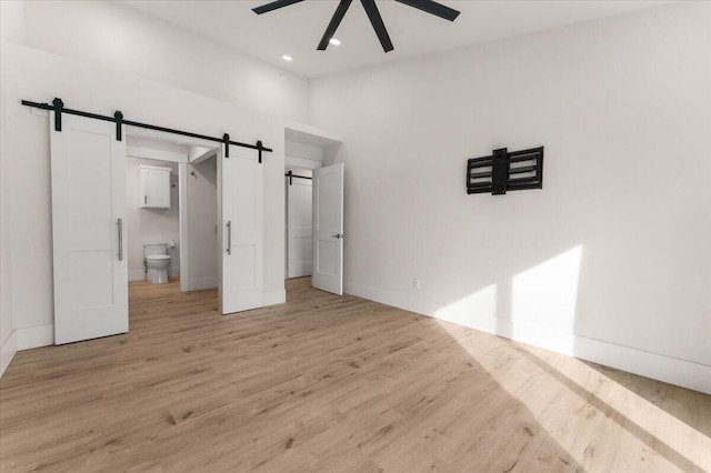 unfurnished bedroom with light wood-type flooring, baseboards, recessed lighting, and a barn door