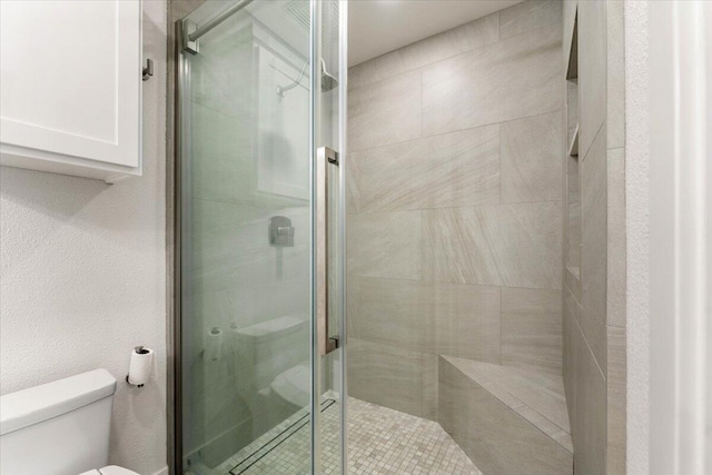 bathroom with a textured wall, a shower stall, and toilet