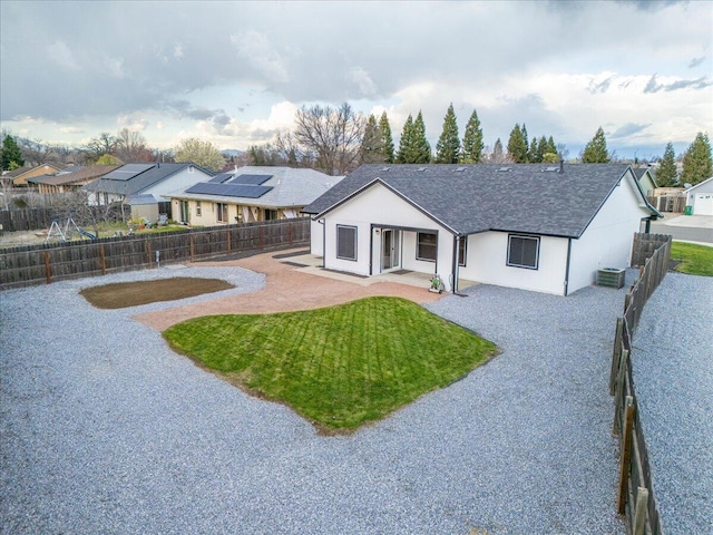 back of house featuring a shingled roof, a lawn, central AC, a residential view, and a fenced backyard