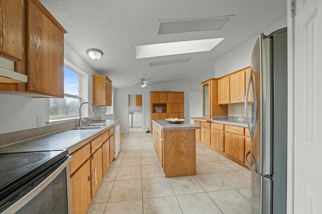 kitchen featuring washer and clothes dryer, light tile patterned floors, stainless steel appliances, a kitchen island, and a sink