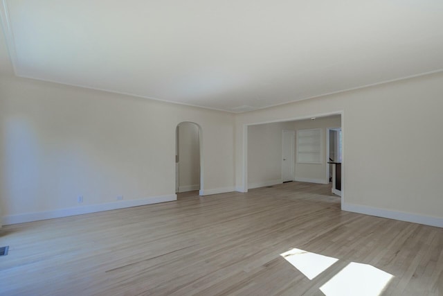 unfurnished room featuring arched walkways, visible vents, light wood finished floors, and baseboards