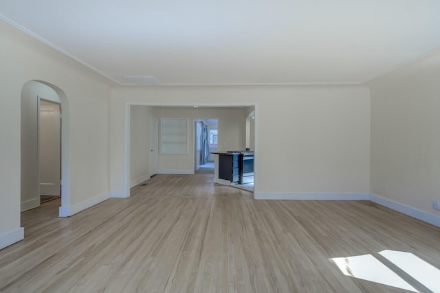 spare room featuring baseboards, arched walkways, and light wood finished floors